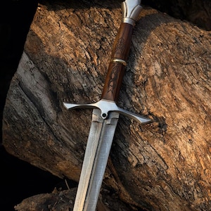 May include: A detailed image of a sword with a silver blade and crossguard. The handle is made of dark wood with intricate carvings and a silver pommel. The sword rests on a weathered wooden surface, showcasing its craftsmanship.