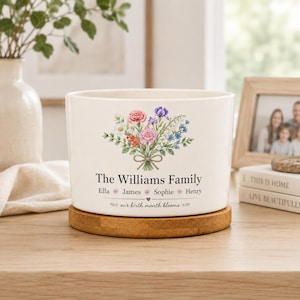 May include: A white ceramic planter with a bamboo base featuring a colorful floral bouquet illustration. The text reads The Williams Family, followed by the names Ella, James, Sophie, and Henry, and the phrase our birth month blooms.