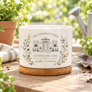 May include: A white ceramic planter with a wooden base featuring a black line drawing of a house, floral accents, and the text: THE ANDERSON HOUSE, 124 WILLOW LANE, new place, new memories. The design is centred on the front of the cylindrical pot.