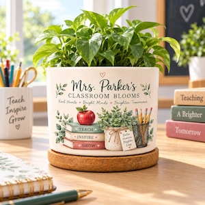 May include: A white ceramic planter containing a green plant, featuring the text Mrs. Parker's CLASSROOM BLOOMS, Kind Hearts, Bright Minds, Brighter Tomorrows, and illustrations of an apple, stacked books, a small potted plant, and pencils.