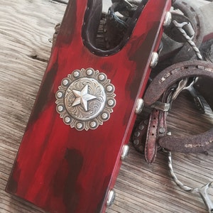 May include: Red wooden boot jack with a silver star concho. The boot jack is distressed and has a rustic look.