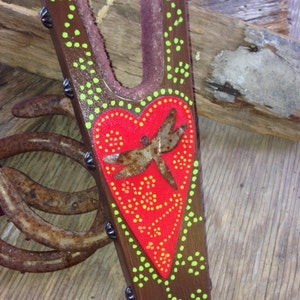 May include: A wooden boot jack with a red heart and a dragonfly design. The heart is decorated with green and orange dots. The boot jack is painted brown and has green and orange dots around the edges.