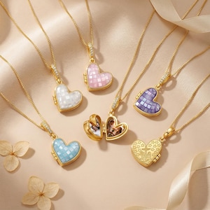 Puede incluir: Collares con colgantes en forma de corazón dorados, con incrustaciones de mosaicos de varios colores. Un medallón está abierto, revelando fotos. Los collares tienen cadenas delicadas y se exhiben sobre un fondo neutro con cintas y flores.