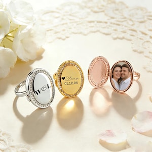 May include: An assortment of oval locket rings in silver, gold, and rose gold. One ring is open, displaying a photograph of a couple. The gold ring is engraved with the name "Lana" and the date "01.12.26". Each ring features a border of small, clear stones.