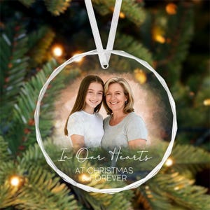 Puede incluir: Un adorno navideño de cristal transparente y facetado con una foto de dos mujeres sonriendo. El adorno tiene el texto "In Our Hearts AT CHRISTMAS & FOREVER" en escritura blanca y cuelga de una cinta blanca.