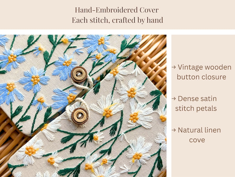 May include: Hand-embroidered cover with blue and white daisy floral design. Features a vintage wooden button closure and dense satin stitch petals. The text reads: Hand-Embroidered Cover. Each stitch, crafted by hand.