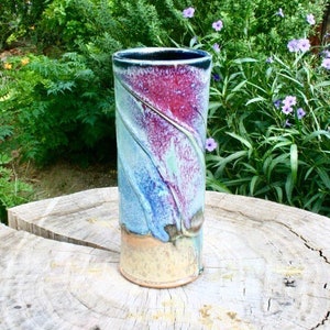 Könnte beinhalten: Eine Keramikvase mit blauer, grüner und violetter Glasur. Die Vase steht auf einem Baumstumpf.