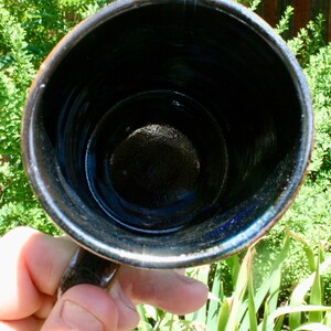 May include: A black ceramic mug with a dark blue glaze inside. The mug is empty and has a smooth, rounded interior.