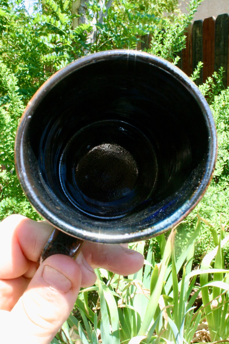 May include: A black ceramic mug with a dark blue glaze inside. The mug is empty and has a smooth, rounded interior.