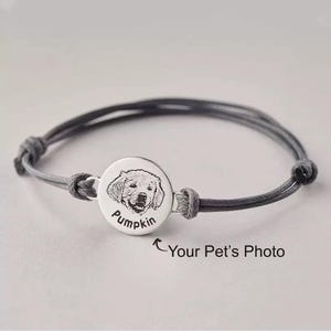 May include: A gray adjustable bracelet featuring a circular pendant with a detailed engraving of a dog's face and the name "Pumpkin". The pendant is connected to the bracelet with gray cords. The text "Your Pet's Photo" is also visible.