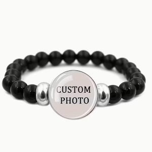 May include: Black beaded bracelet with a central circular charm. The charm has the text "CUSTOM PHOTO" in black. The bracelet features black, round beads and silver-coloured spacers. The bracelet is designed to be worn on the wrist.
