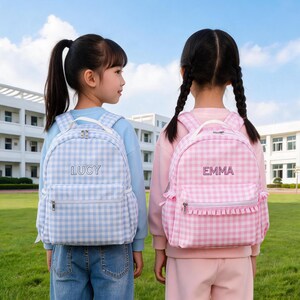 May include: Two backpacks with a gingham pattern, one in light blue with the name LUCY embroidered in white, and one in light pink with the name EMMA embroidered in white. Both backpacks feature a front zippered pocket and top handle.