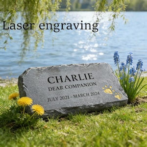 Könnte beinhalten: Ein grauer Gedenkstein für Haustiere mit dem Namen "CHARLIE", den Worten "DEAR COMPANION" und den Daten "JULI 2021 - MÄRZ 2024". Auf der rechten Seite befindet sich ein goldener Pfotenabdruck. Der Text "Laser engraving" steht oben.