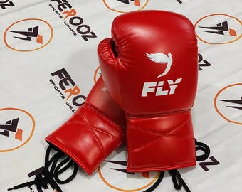 Könnte beinhalten: Ein Paar rote Boxhandschuhe mit dem Wort "FLY" und einem weißen Flügel-Logo auf der Vorderseite. Die Handschuhe sind mit schwarzen Schnürsenkeln geschnürt. Der Hintergrund ist weiß mit dem Text "FEROOZ SPORTS WEARS".
