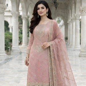 May include: A light pink salwar kameez ensemble. The outfit includes a long-sleeved tunic with intricate gold embroidery, matching wide-leg pants, and a sheer dupatta. The outfit is worn with gold earrings and a bracelet.