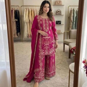 Puede incluir: Conjunto salwar kameez magenta bordado en oro. El atuendo incluye una túnica de manga larga, pantalones de pernera ancha y una bufanda a juego. El bordado dorado adorna el cuello, las mangas y los pantalones. Zapatos dorados completan el look.