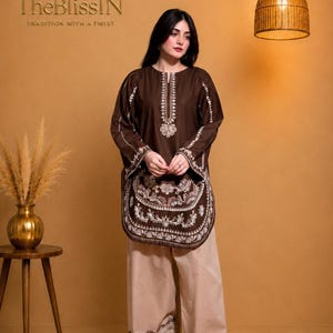 May include: A dark brown long-sleeved tunic featuring white floral embroidery along the neckline, sleeves, and hem, paired with wide-leg beige trousers that have a matching embroidered border at the bottom cuffs.