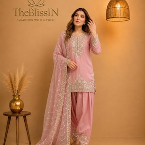 Puede incluir: Un conjunto de salwar kameez en color rosa empolvado que presenta una túnica de manga larga con intrincados bordados plateados alrededor del cuello y el dobladillo, junto con pantalones plisados y una dupatta transparente bordada.