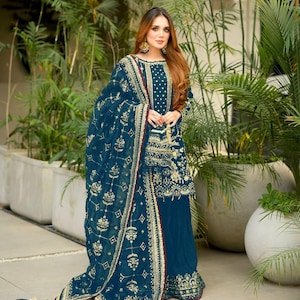 May include: A teal salwar kameez with gold embroidery. The outfit includes a tunic, trousers, and a dupatta. The dupatta is draped over the shoulders. The ensemble is decorated with gold thread and accessorized with gold earrings.