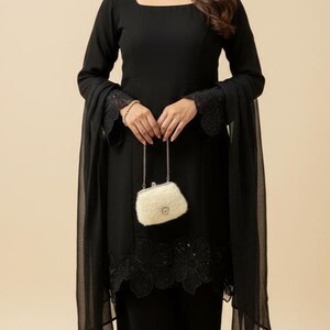 May include: A black ensemble featuring a long-sleeved top with a square neckline and matching pants. The outfit includes a sheer scarf and a small, fluffy, off-white purse. The sleeves and pant hems are adorned with lace detailing.