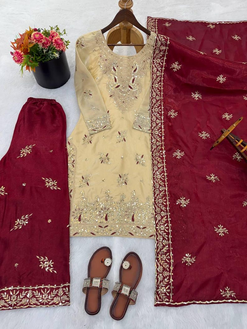 Puede incluir: Un conjunto salwar kameez bordado de color crema, con un dupatta y pantalones burdeos a juego. El conjunto incluye una t&uacute;nica de manga larga con intrincados adornos dorados y plateados. Tambi&eacute;n se incluyen sandalias de cuero marr&oacute;n con detalles plateados.