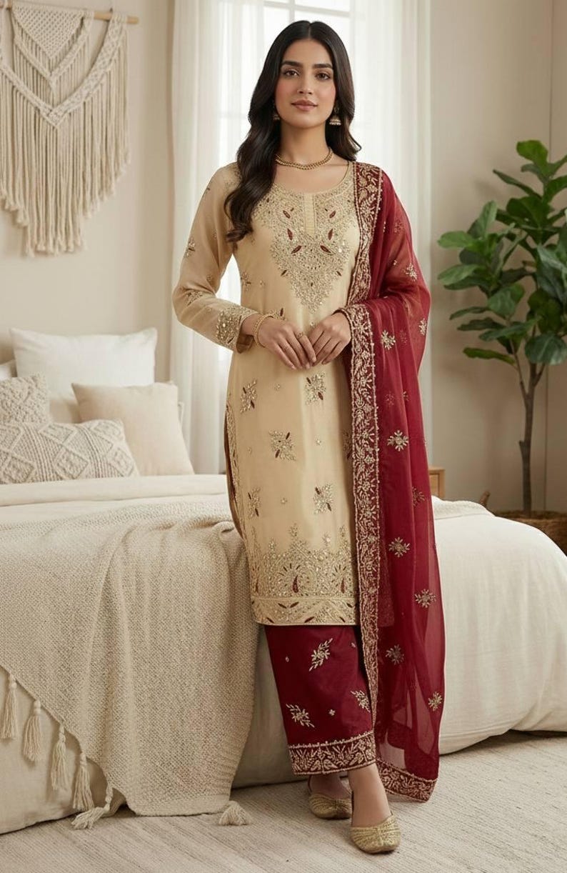 Puede incluir: Un conjunto salwar kameez beige bordado con un dupatta granate. La t&uacute;nica y el pantal&oacute;n de manga larga est&aacute;n adornados con intrincados bordados dorados. La bufanda granate transparente tiene un borde dorado. El atuendo es adecuado para ocasiones especiales.