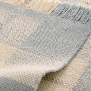 K&ouml;nnte beinhalten: Nahaufnahme eines gewebten Teppichs mit geometrischem Muster. Der Teppich weist abwechselnde Streifen in Hellblau, Off-White und einem Hauch von Braun auf. Die Kanten sind mit einem Fransenbesatz in passenden Farben versehen, der Textur und Detail verleiht.