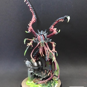 May include: A detailed miniature figure of a creature with a dark blue and red exoskeleton, multiple limbs, and large, clawed appendages. The figure is painted with green accents and stands on a base with a green, toxic-looking substance.