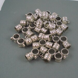 May include: A pile of silver-toned metal bead caps with a ridged design. The caps have a small loop on the top for attaching to jewelry.