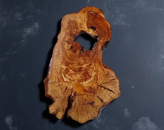 May include: A unique, irregularly shaped wooden slab with a natural edge. The wood has a warm, golden-brown hue with intricate grain patterns and a central hole. The slab is likely a decorative piece or a serving board.