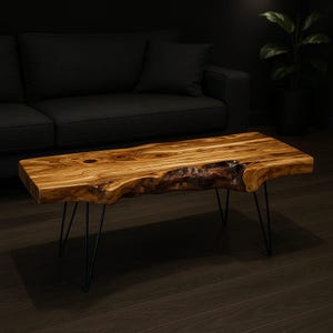 May include: A live edge coffee table with a natural wood grain finish. The table has a rectangular shape with a unique, organic edge. It is supported by black metal hairpin legs, adding a modern touch to the rustic design.