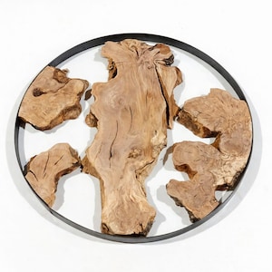Op de afbeelding: Een decoratief wandkunstwerk met natuurlijke houten schijven gerangschikt in een zwarte metalen ring. De houten stukken hebben een lichtbruine kleur en unieke texturen, wat een rustieke en organische uitstraling creëert. Het cirkelvormige ontwerp voegt een moderne touch toe.