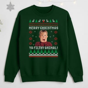Può includere: Una felpa verde scuro con un design festivo. Il design include il testo "MERRY CHRISTMAS YA FILTHY ANIMAL!" sopra l'immagine di un bambino sorpreso. Il design presenta anche renne, alberi di Natale e fiocchi di neve.