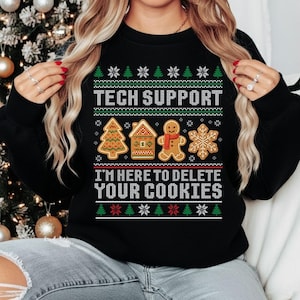 May include: Black sweatshirt with a festive Christmas design. The text "TECH SUPPORT" and "I'M HERE TO DELETE YOUR COOKIES" are displayed above and below gingerbread house, tree, man, and snowflake graphics.