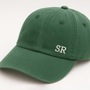 Peut inclure: Casquette de baseball verte avec une visière incurvée. Le chapeau porte les lettres blanches "SR" brodées sur le devant. La casquette est en tissu doux et possède un bouton sur le dessus.