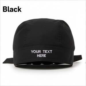 Puede incluir: Gorra negra con el texto "YOUR TEXT HERE" en blanco. La palabra "Black" est&aacute; impresa en la esquina superior izquierda. La gorra tiene una corona redondeada y lazos en la parte trasera.