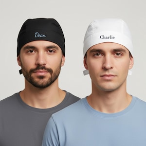 Puede incluir: Dos gorros quir&uacute;rgicos, uno negro y otro blanco. El gorro negro tiene el nombre "Dean" bordado en una escritura azul claro, mientras que el gorro blanco tiene "Charlie" en el mismo estilo. Ambos gorros se muestran en personas que visten camisas de color s&oacute;lido.