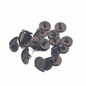 May include: A collection of black earring posts with flat, round settings. The earring posts are scattered against a white background, showcasing their simple, yet elegant design. These earring components are ideal for DIY jewelry projects.
