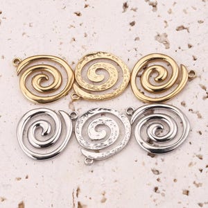 May include: Six metal spiral charms in gold and silver tones. The gold charms have a hammered texture, while the silver ones are smooth. Each charm has a small loop for attaching to jewelry or other crafts. The charms are arranged in two rows of three.