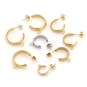 May include: A collection of gold-colored and silver-colored hoop earrings. The earrings are in various stages of assembly, with some featuring posts and others with open loops for attaching additional elements. The earrings are on a white background.