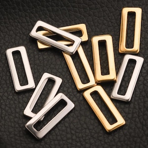 以下が含まれることがあります： 金と銀色の長方形の金属バックルのコレクション。 バックルはシンプルなオープンフレームデザインで、黒いテクスチャの表面に散らばっています。 これらのハードウェアコンポーネントは、おそらく、工芸品やファッションアクセサリー用です。