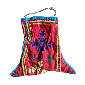 May include: A red textile bag with a geometric design in blue, green, and yellow. The bag has a blue trim and a purple cord for hanging. The bag is likely handmade and features embroidered details.
