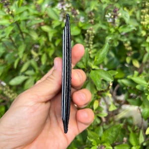 Puede incluir: Una cartera delgada de cuero negro con separadores de tarjetas blancos se sostiene frente a un fondo de hojas verdes. La cartera parece compacta y est&aacute; dise&ntilde;ada para guardar tarjetas y efectivo.