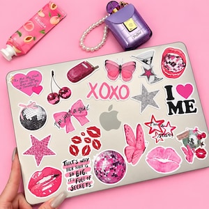 May include: A silver laptop covered in various pink and glittery stickers including disco balls, butterflies, lips, stars, cherries, and text phrases like XOXO, I love me, and quotes about hair and secrets, with a peach tube and purple perfume nearby.