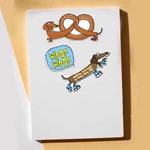 May include: A white sticker sheet featuring two dachshund dog illustrations. One dog is paired with a pretzel, the other is on roller skates with the text "Rolling through a long day like". A blue speech bubble says "Woof Woof".