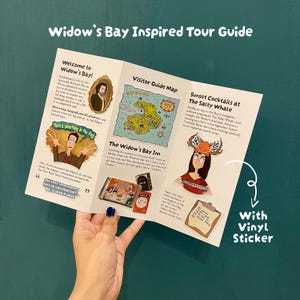 Op de afbeelding: Een drieluik Widow's Bay Inspired Tour Guide brochure met een kaart, tekst en illustraties van personages en locaties. De brochure bevat een vinylsticker van een persoon met een gewei-hoofdband die een kom vasthoudt.