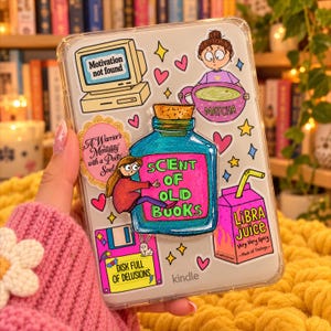 Può includere: Una custodia trasparente per Kindle decorata con vari adesivi colorati, tra cui una bottiglia blu con l'etichetta Scent of Old Books, un cartone di succo rosa Libra Juice, un monitor con Motivation not found e un floppy disk con Disk Full of Delusions.