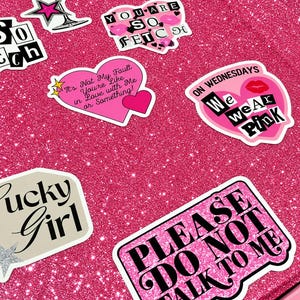 May include: A bright pink glittery surface covered in various stickers including a martini glass, a pair of lips, and heart-shaped designs with text such as "You are so fetch," "It's not my fault you're like in love with me," and "Please do not talk to me."