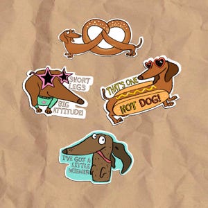 May include: A collection of four dachshund stickers. One sticker shows a dachshund with a pretzel, another with star-shaped sunglasses and the text "SHORT LEGS BIG ATTITUDE!", another with heart-shaped sunglasses and a hot dog, and the last with the text "I'VE GOT A LITTLE WIENER".