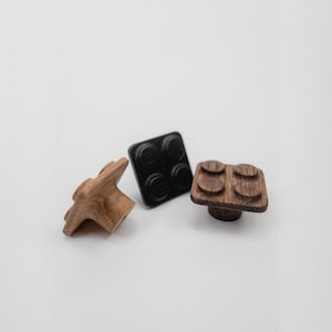 May include: Three wooden cabinet knobs in different designs. One is a star shape, another is a black square with four circular indentations, and the third is a square with four circular indentations in a wood grain finish.